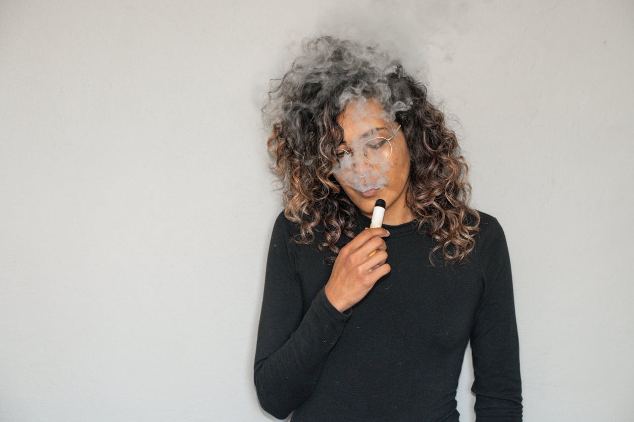 Portrait of a woman with curly hair vaping indoors, featuring smoke and a relaxed expression.