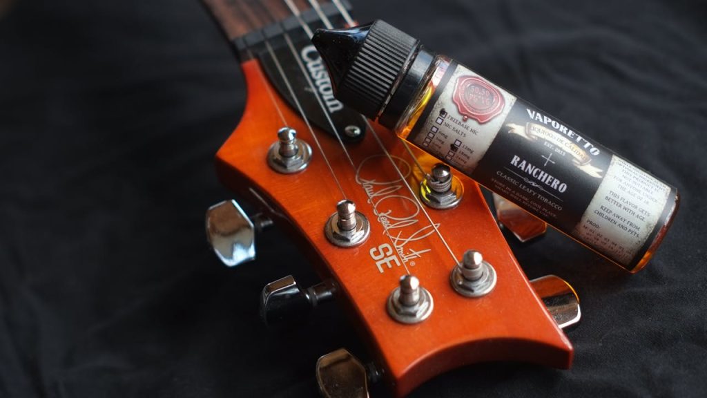 Mastering the First Impression: Your intriguing post title goes here Close-up of a guitar headstock paired with a Vaporetto e-liquid bottle, showcasing music and vaping lifestyle.