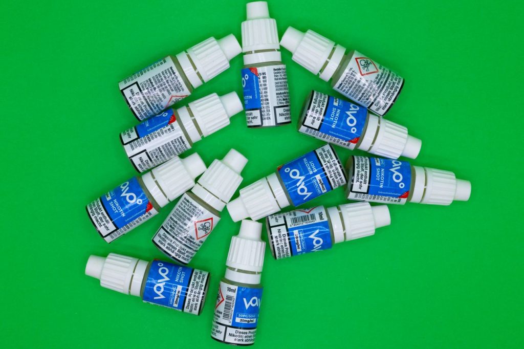 Crafting Captivating Headlines: Your awesome post title goes here Top view of multiple nicotine vape shot bottles arranged on a green background.