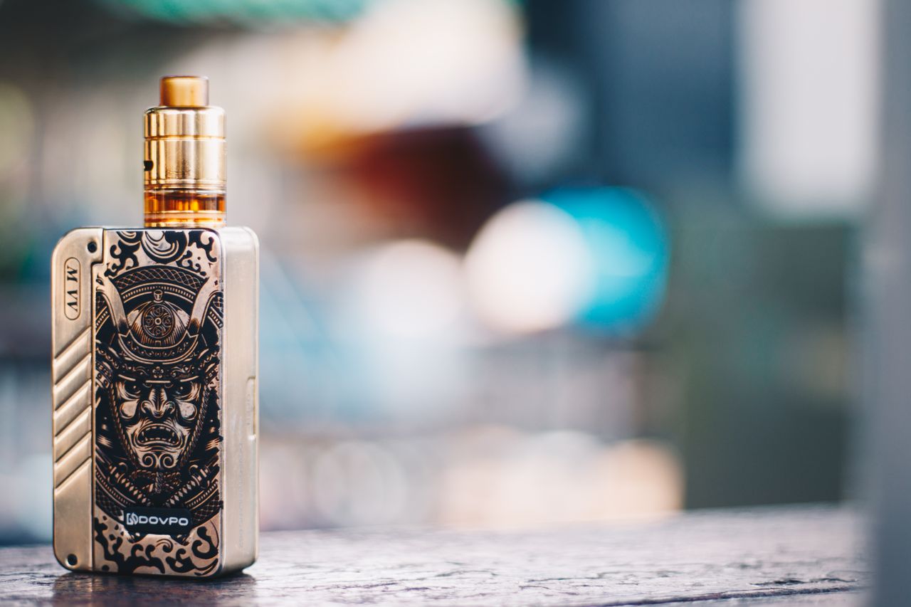 our-story-02 Close-up of a vape device with samurai design, set against a blurred background in Bangkok.