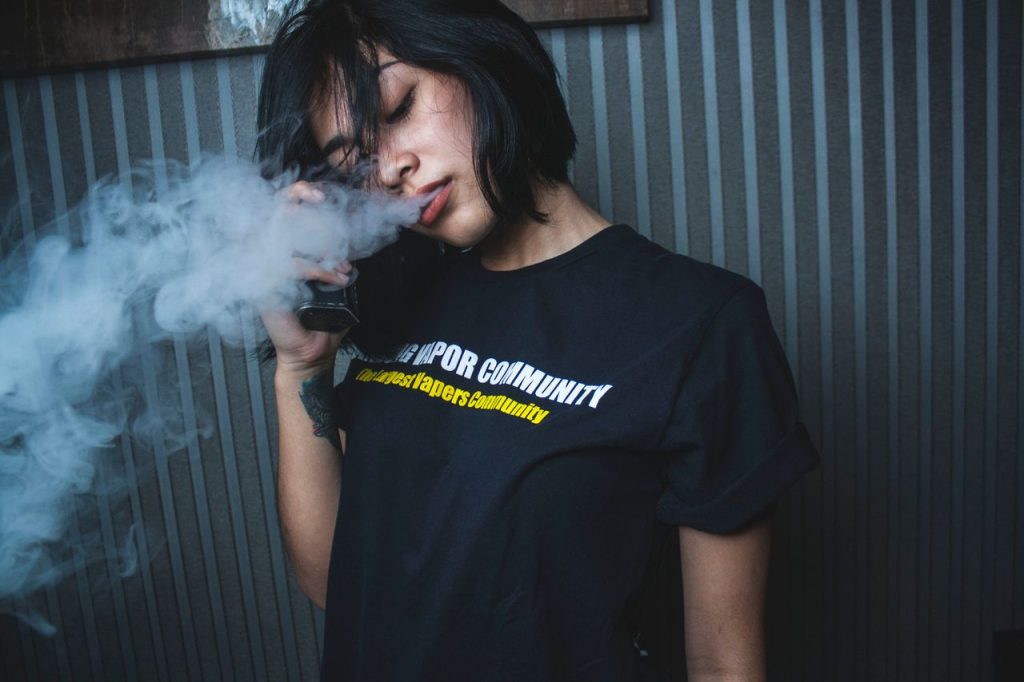 Calm young ethnic female in casual clothes smoking electronic cigarette with closed eyes